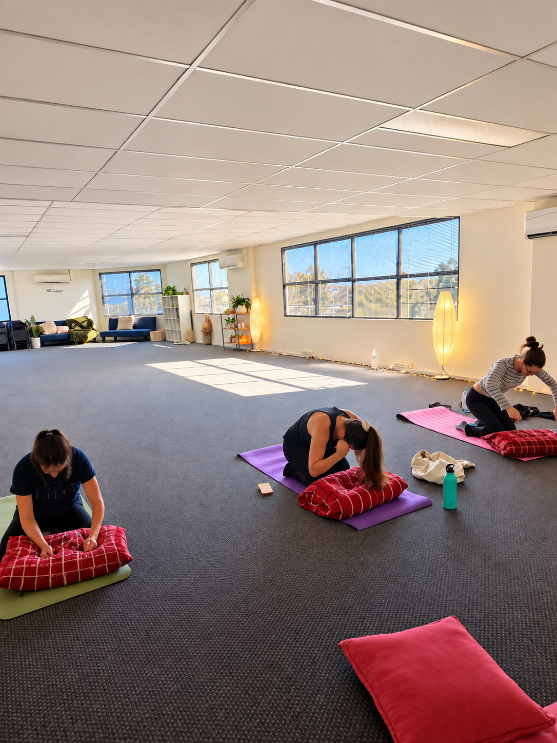 Women kneeling on mats, punching red pillows in a bright studio
